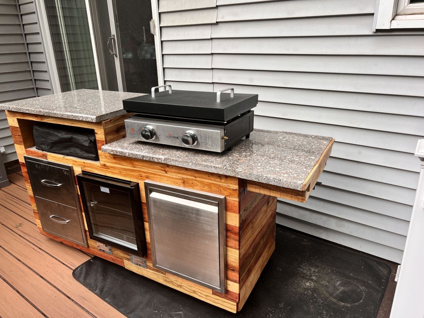 The finished grill cart on the deck with griddle, fridge, drawers and granite tops